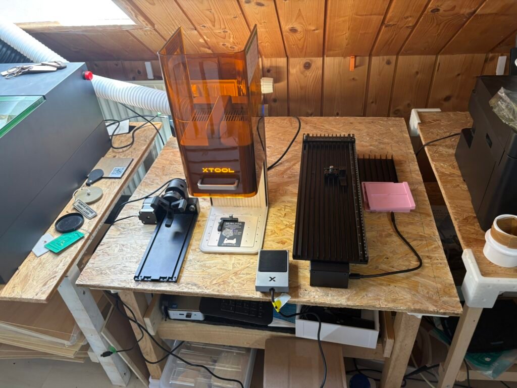 Orange-trost 3D printer in a wood-paneled workshop, with a black accessory rail and power cables on a plywood workbench